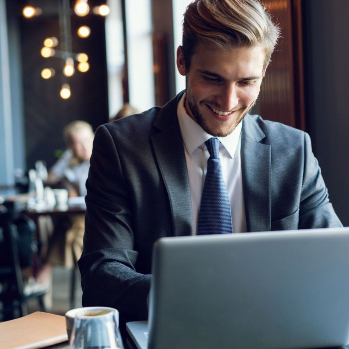 Attractive businessman using a laptop and smiling while working in cafe