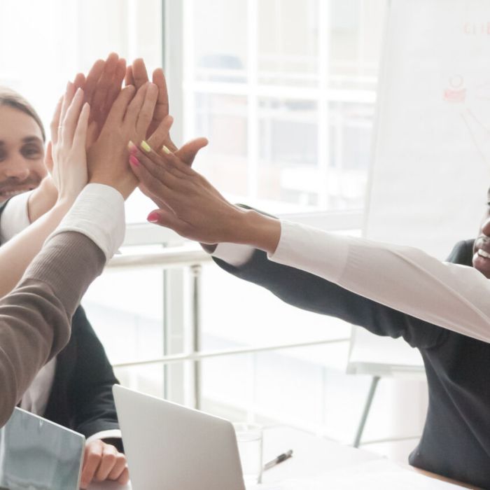 Diverse businesspeople sitting at desk celebrating success giving high five